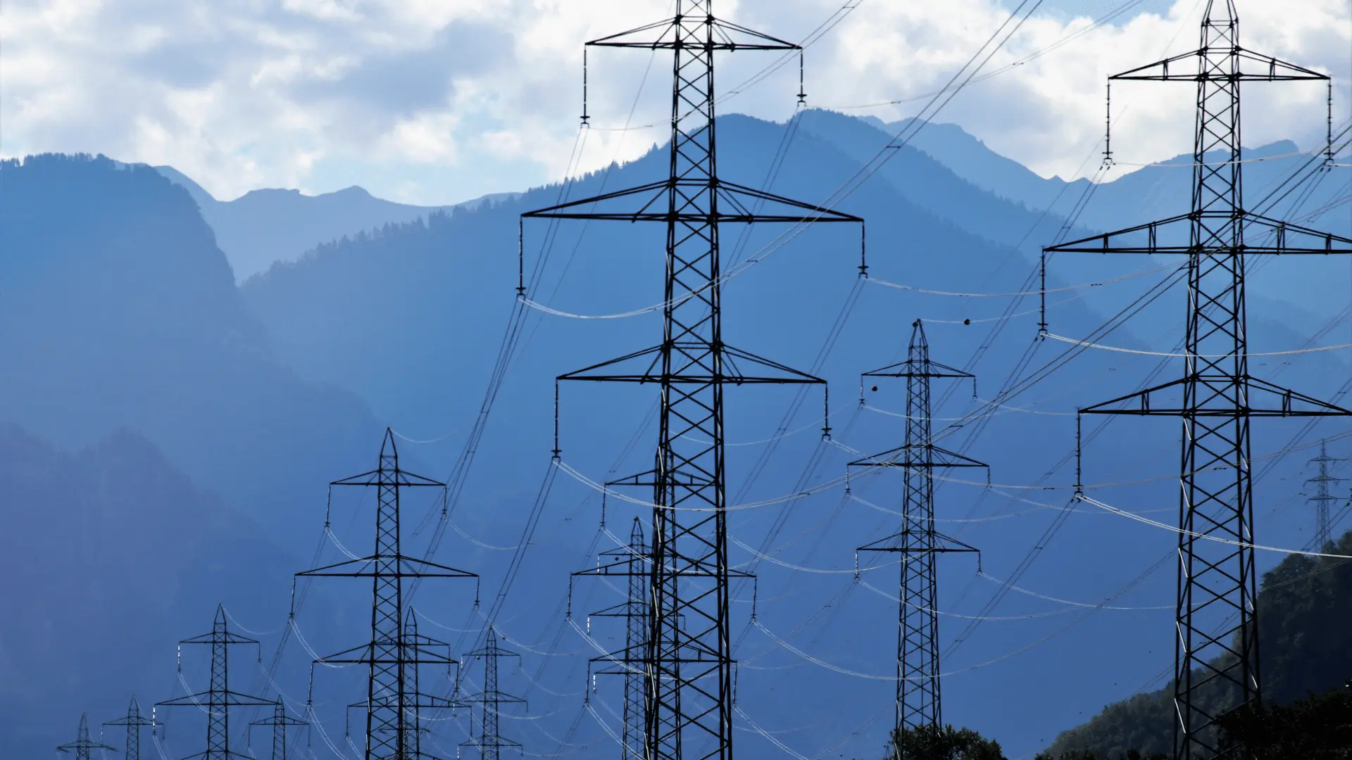High-voltage electricity transmission towers set against blue misty mountains, representing power system engineering and grid infrastructure.